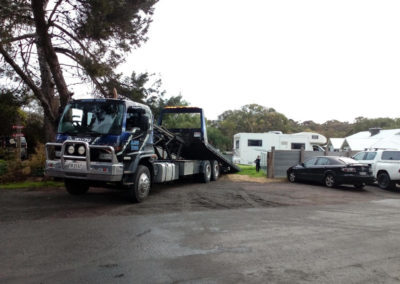 A large tilt tray tow truck unloading a caravan